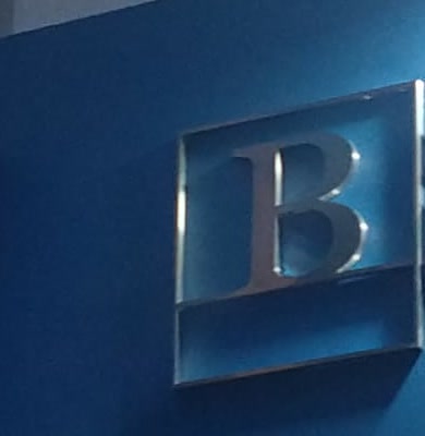 Logo de Nuevo Chaco Bursátil en letra corpórea de acero inoxidable dentro de un marco cuadrado, sobre una pared azul